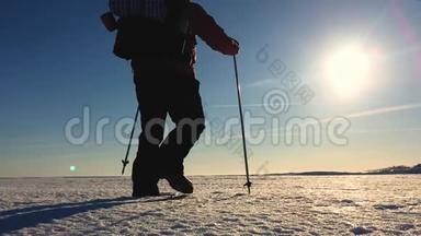 穿着雪鞋在冬天的风景中行走的人的剪影。 带着徒步旅行杆，蓝天和